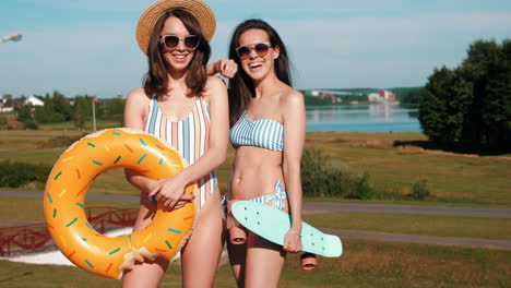 two friends enjoying summer at the park with swimsuits, float, and skateboard