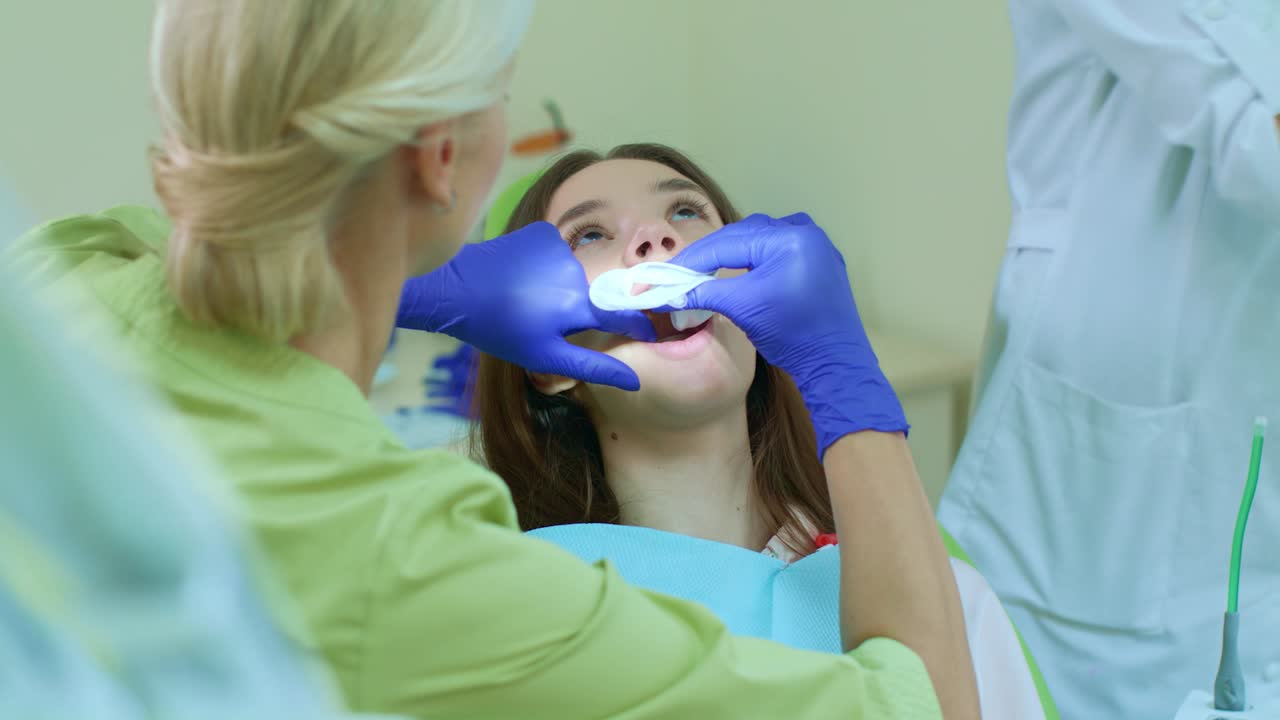 Dentist with assistant preparing girl for whitening teeth. Whitening procedure