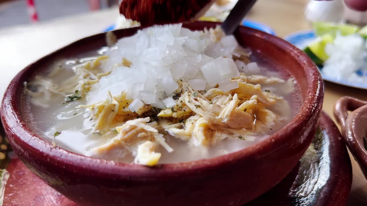 Preparing a bowl of spicy pozole with chili peppers and spices