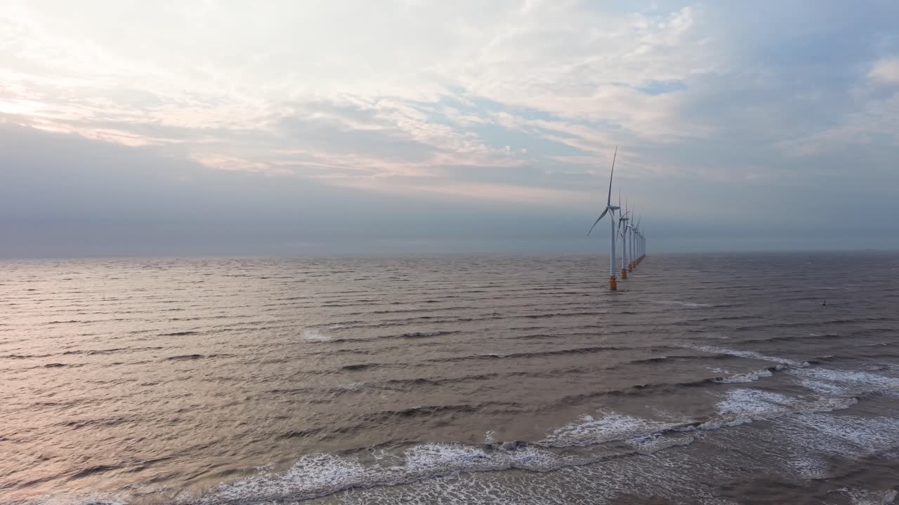 Le turbine eoliche generano energia al largo della costa di Tra Vinh, Vietnam, nella luce della sera vicino alla riva.