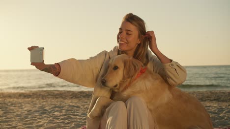 a girl takes a selfie together with her big cute dog of light coloring in the morning against the backdrop of a sunny beach