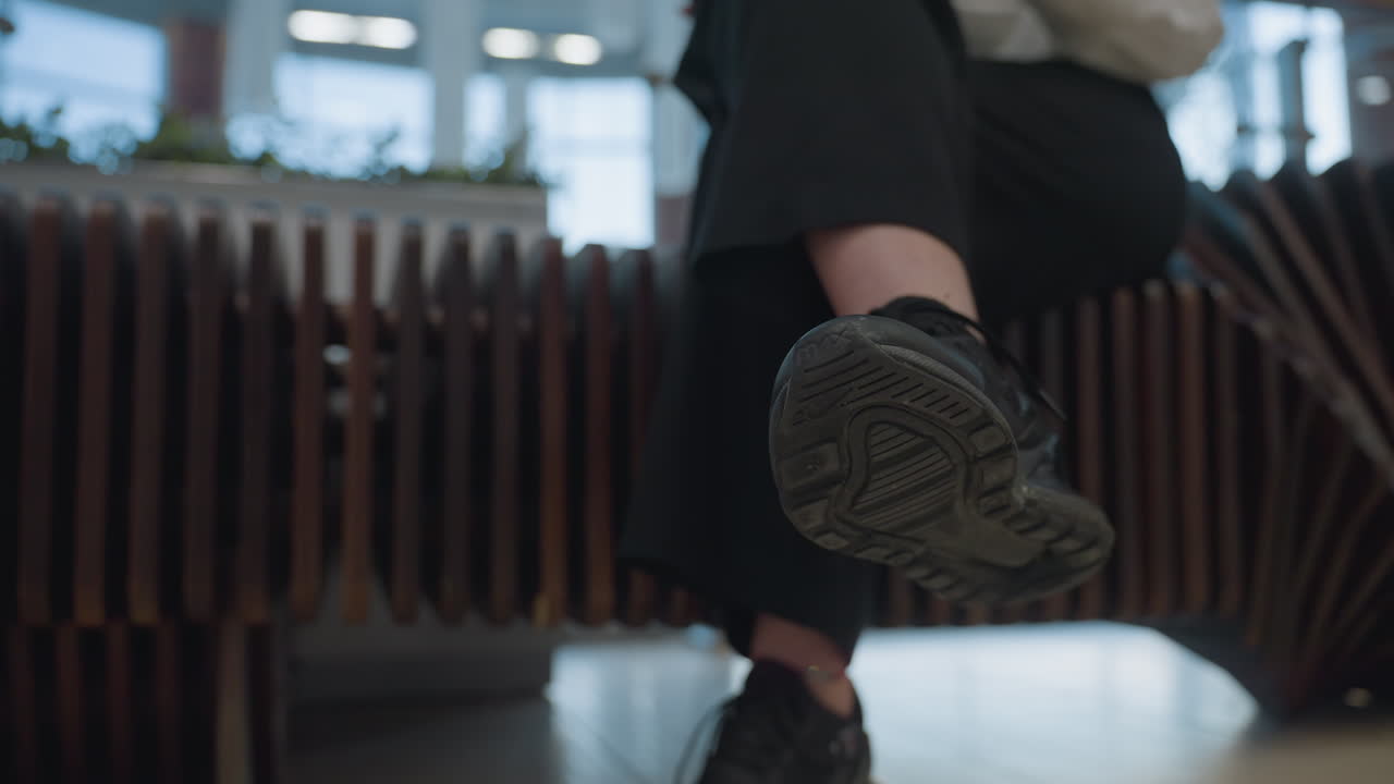 Close up of lady crossing leg while seated, gently tapping foot to rhythm of music. Scene shows modern bench detail and motion suggesting calm mood in indoor public space