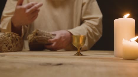 studio shot of man wearing robes representing figure of jesus christ breaking and offering bread