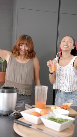 vertical video: smiling women in kitchen making fresh juice with blender and enjoying drinks