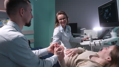 pregnant woman having ultrasound scan at the gynecologist office while loving husband holding her hand 9