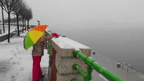 Child-holding-vibrant-colorful-umbrella-and-red-gloves-plays-with-snow,-Italy