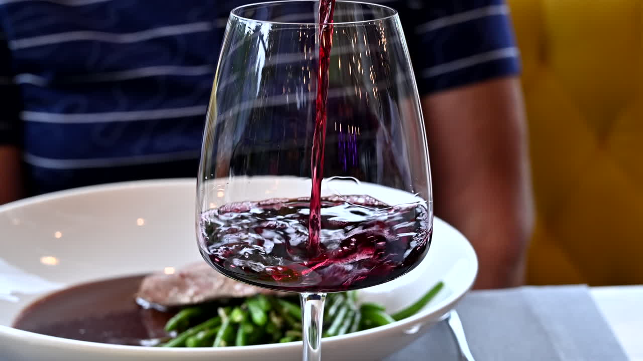 Uomo che versa vino rosso in un bicchiere a un tavolo in un ristorante