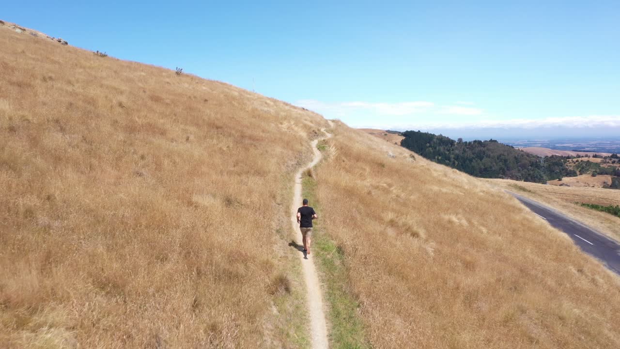 Tracking drone shot of man running on single trail with blue sky in background