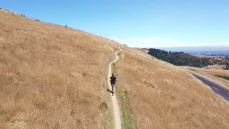 tracking drone shot of man running on single trail with blue sky in background