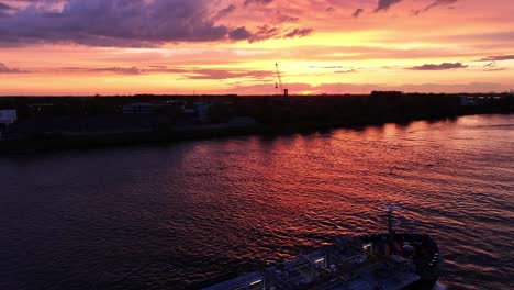 Colourful-dramatic-sky,-land-silhouettes,-rippling-water,-container-vessel