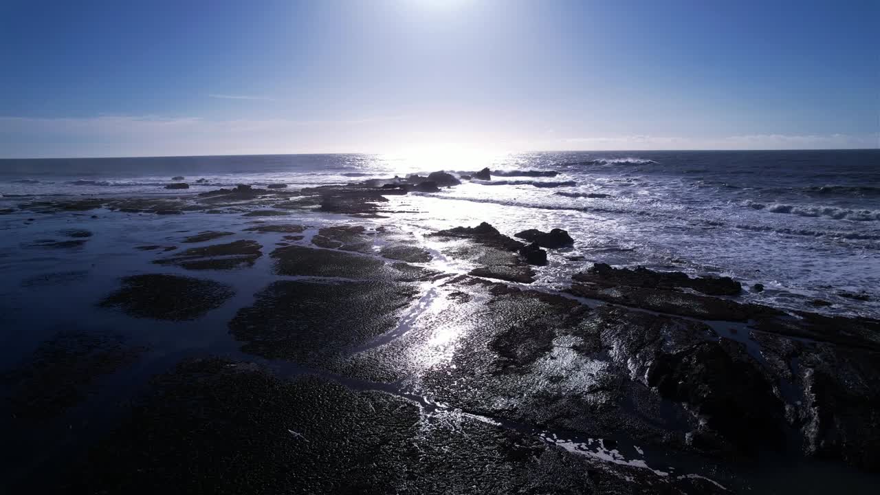 drone vuela sobre formaciones rocosas y pozas de marea en mavericks beach, california durante la puesta de sol