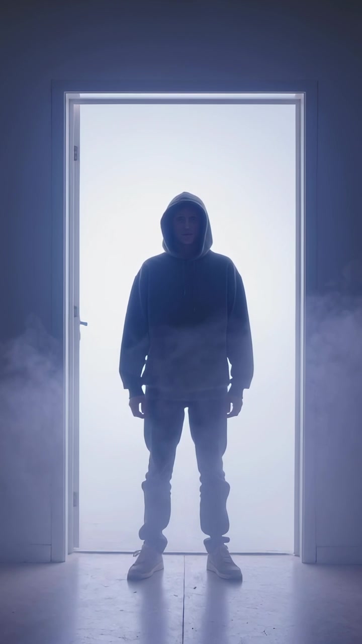 Video verticale: Retroilluminazione che si attiva, uomo con la felpa in piedi sulla porta dello studio per una rivelazione con nebbia