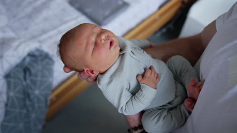 adorable tiny baby boy in hands of a man. newborn sleeping peacefully rocked by the father. close up.