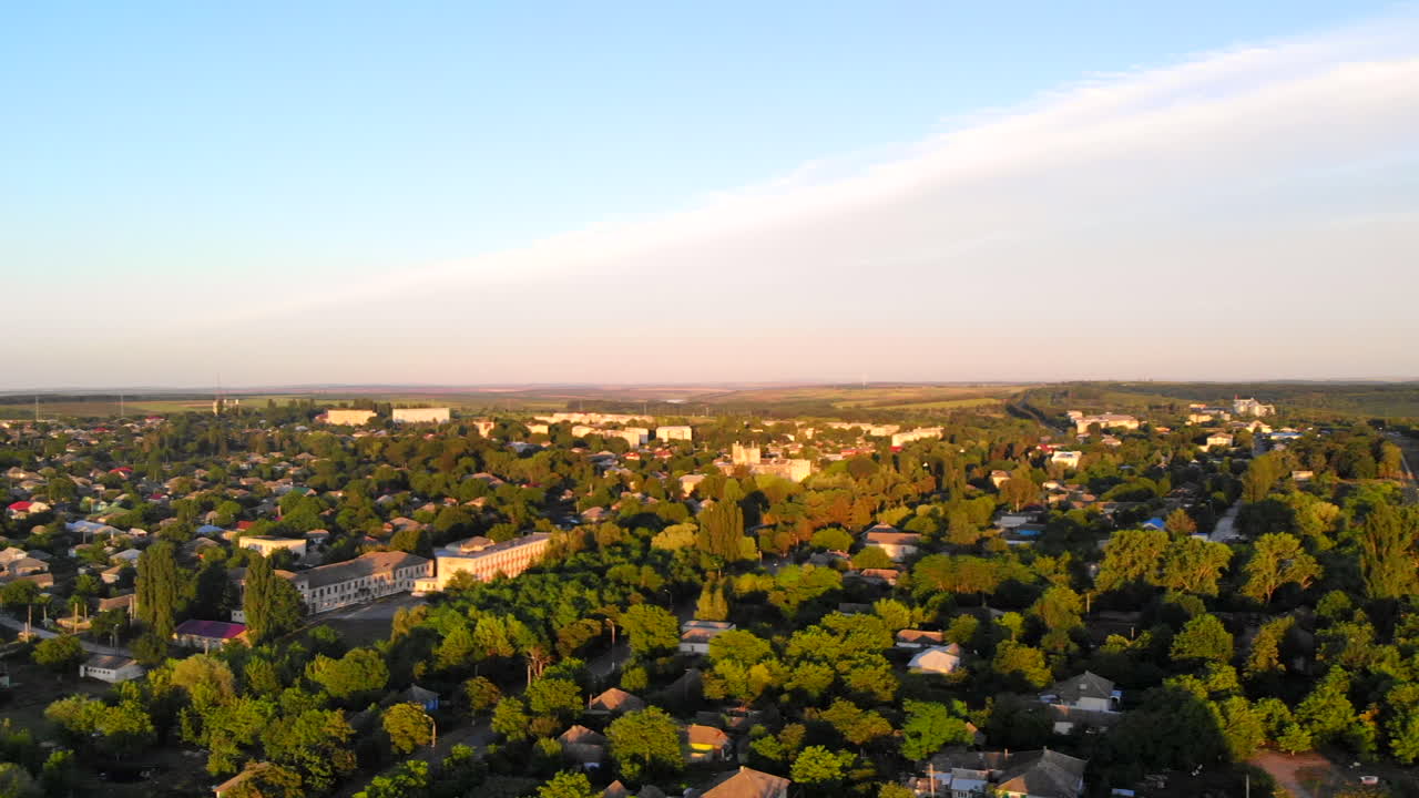 Aerial drone shot of Donduseni city with multiple residential buildings and greenery and fields. Sunset in Moldova