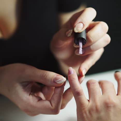 master of manicure is holding the client's finger and covering the nails with a gel polish in the beauty salon