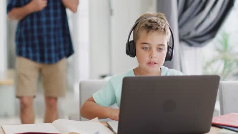 Happy-caucasian-boy-sitting-at-table-and-using-laptop-for-online-lesson,-slow-motion