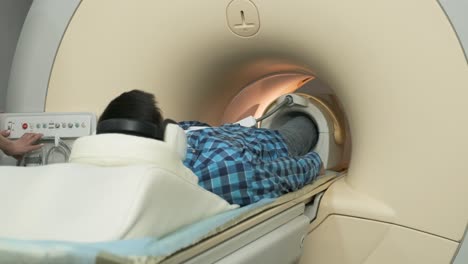 mujer médico hace escaneo de resonancia magnética de la articulación de la rodilla. joven paciente en mesa automática moviéndose fuera de la máquina de resonancia eléctrica de tipo cerrado usando auriculares de aislamiento de ruido. equipo moderno, bobina en la rodilla del paciente