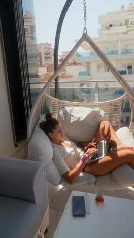 woman working on a laptop on a balcony hanging chair