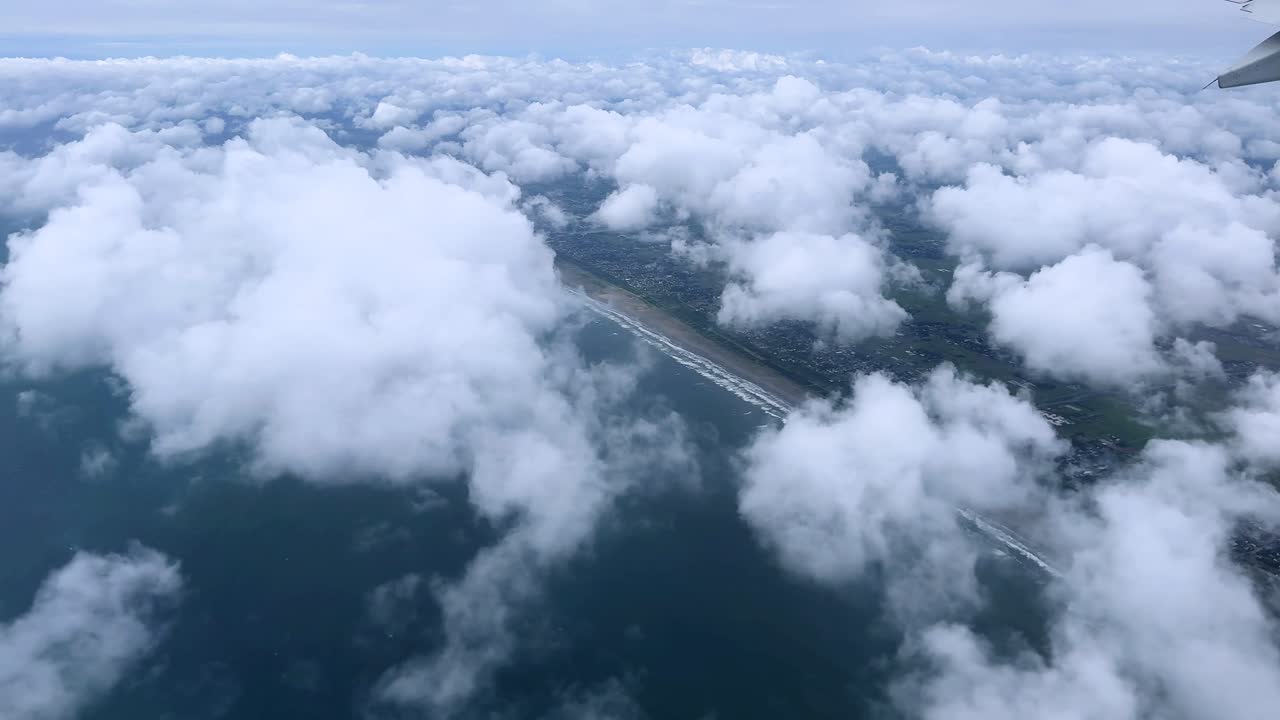 View of fluffy clouds and coastline from an airplane window flying over the ocean below