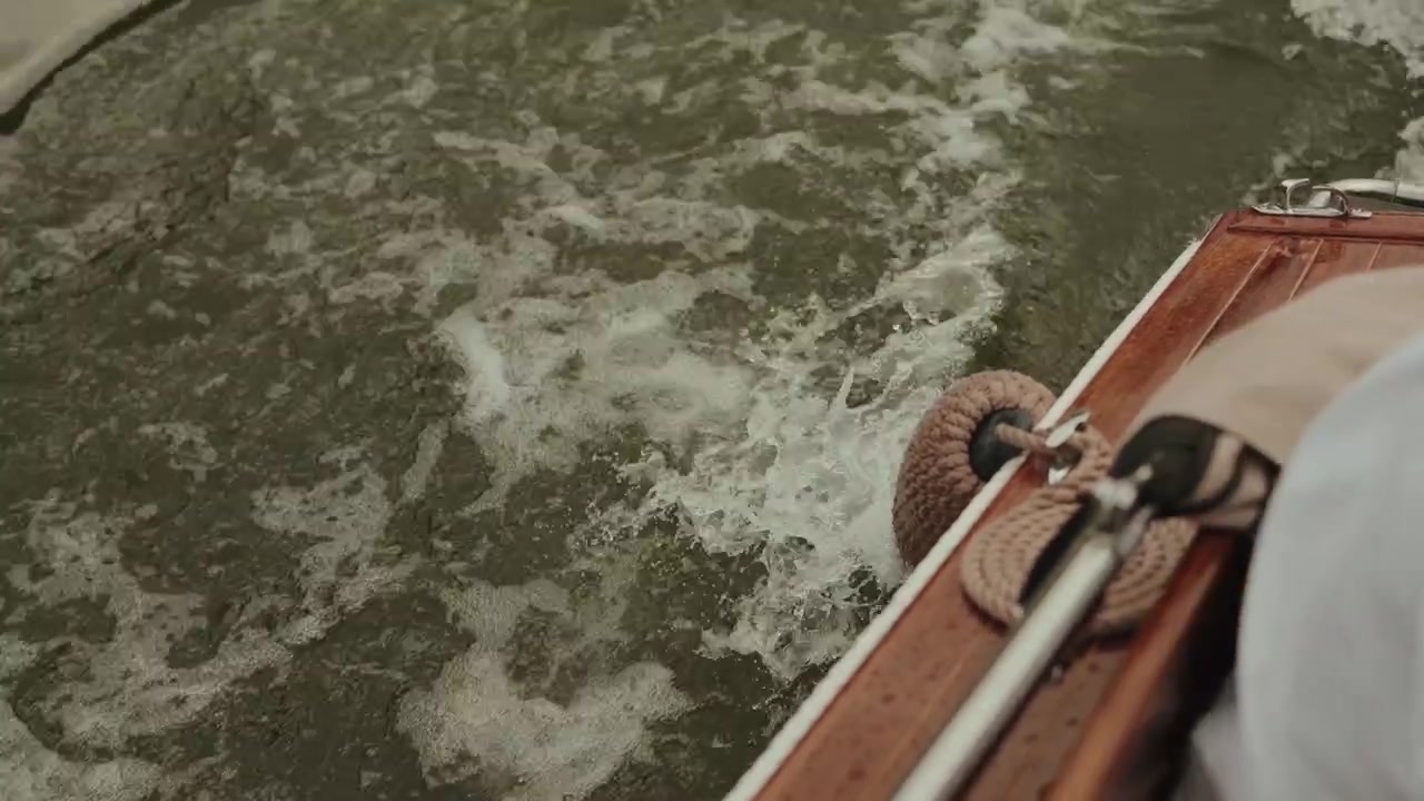 Acqua torbida e marrone del fiume che si agita accanto allo scafo in legno di una barca in movimento con parabordi in corda