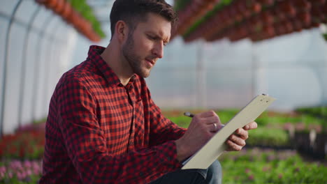 gardener analyzing and noting plant status in greenhouse
