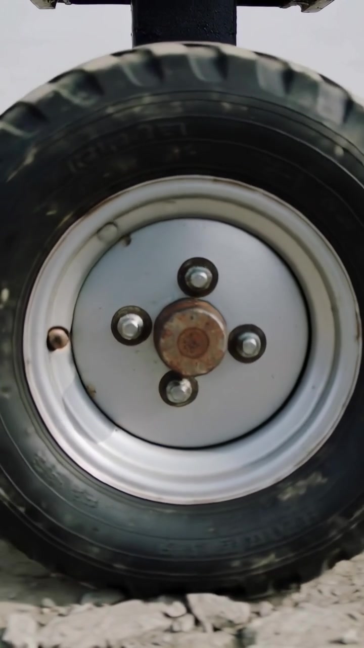 Vertical video: Camera shifting revealing utility wheel in bay, showing rusted spindle and lug nuts