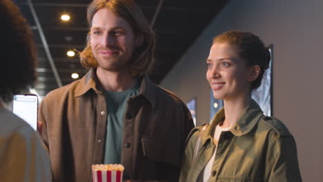 happy couple with popcorn box showing qr movie ticket on a cell phone at the cinema