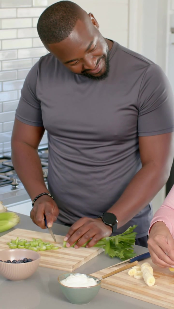 Video verticale: Uomo in maglietta grigia che taglia il sedano con un coltello da chef in cucina, iniziando la preparazione.