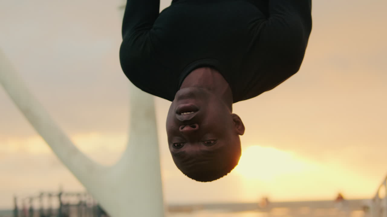 African American Man Hanging Upside Down Against Golden Sunset Sky