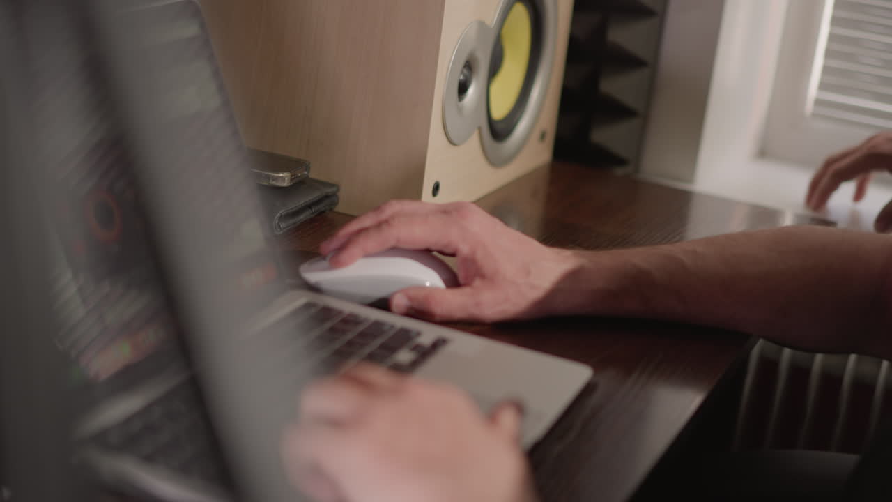 한 손은 키보드 위에, 다른 손은 마우스 위에 놓여 노트북에서 작업하는 손의 클로즈업 으로, 이 장면에는 흐릿한 배경과 테이블 위에 다른 사람의 손이 있습니다.