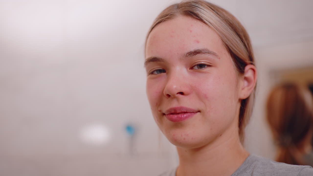Primo piano di una giovane donna in bagno che si asciuga delicatamente il viso con un morbido asciugamano beige dopo averlo lavato, sorridendo dolcemente con un'espressione naturale, mettendo in risalto la skincare quotidiana