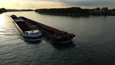 un buque de carga con una barcaza lateral que pasa por el río al atardecer