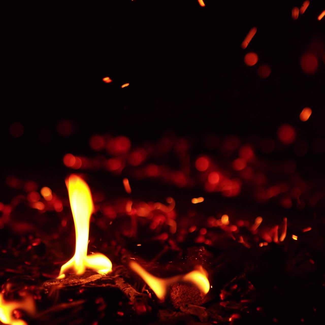 Tapping by the hot smoldering embers. Bright sparks fly up and little flames appear. Close up
