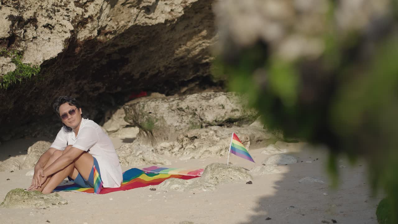 Man Relaxing on the Beach with Rainbow Flag