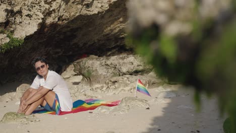 man relaxing on the beach with rainbow flag