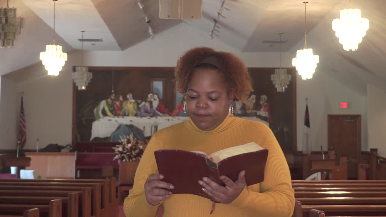 joven afroamericana leyendo felizmente la biblia en una iglesia vacía durante los cierres