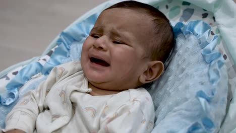 british asian 6 month old baby crying and looking agitated whilst in baby bouncer