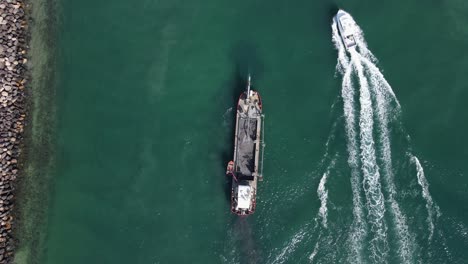 un barco de lujo que pasa por un gran barco industrial de dragado de arena junto a una pared de roca costera