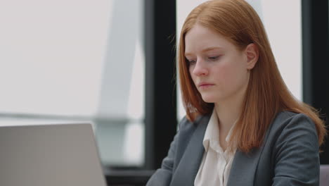 A-young-red-haired-business-woman-looks-thoughtfully-at-the-screen-and-brainstorms.-Watch-and-think-about-problems-looking-out-the-window.-Thoughtful-business-woman