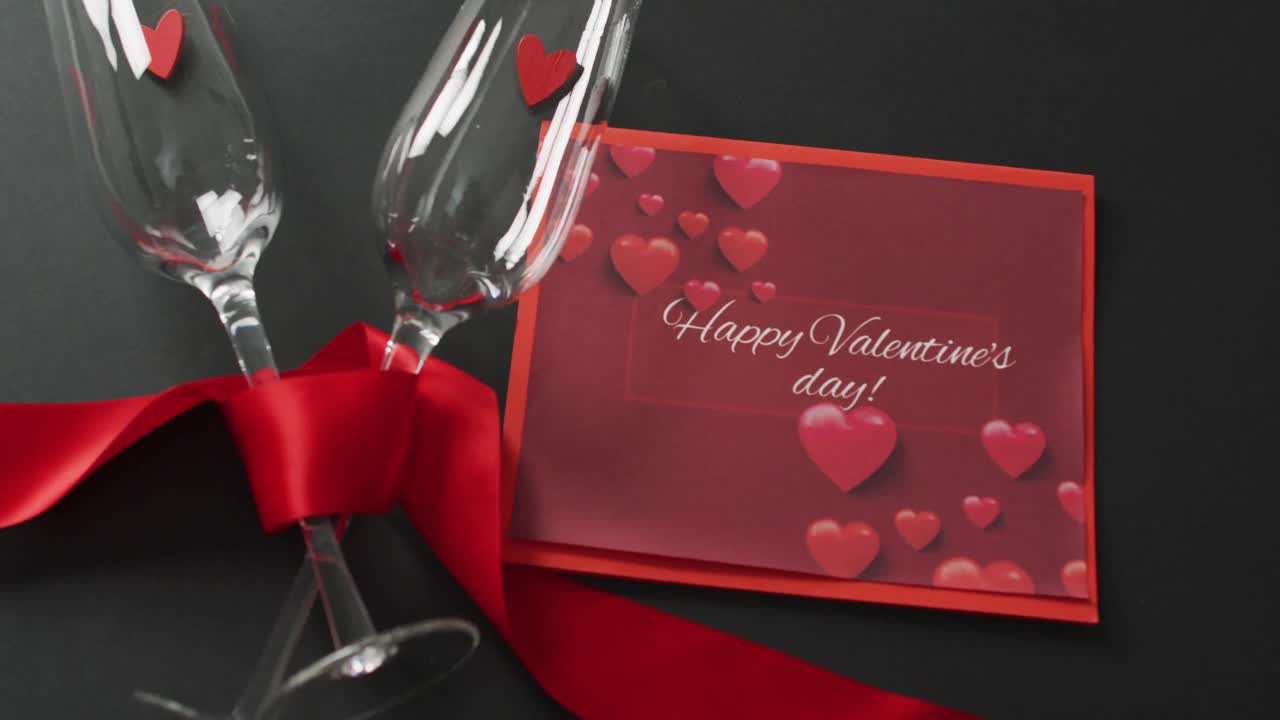 Happy valentine's day text over champagne glasses with hearts and red ribbon
