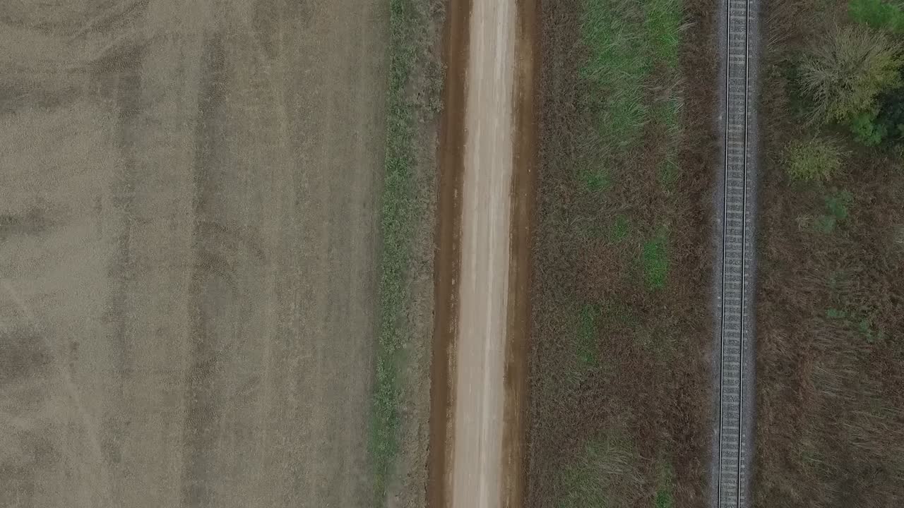 Veduta aerea dall'alto di una strada di campagna con un binario ferroviario sulla destra e un campo coltivato sulla sinistra in Sud America.