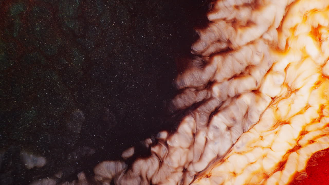 Macro shot of flowing blue, orange, and brown inks creating a shimmering galaxy effect through swirling liquid motion