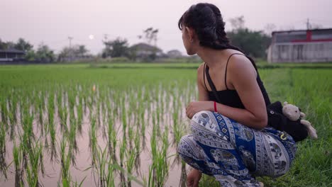 woman crouching by a rice paddy field at dusk