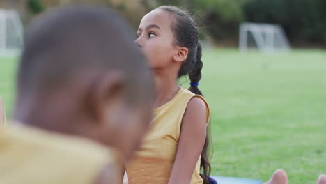 Diverse-group-of-schoolchildren-lying-on-mats-meditating-during-yoga-lesson-outdoors