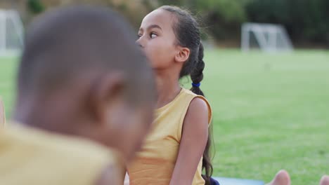 diverse group of schoolchildren lying on mats meditating during yoga lesson outdoors