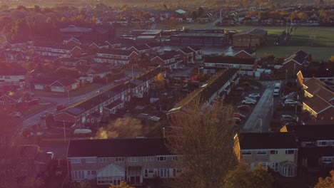 UK-Townhouse-estate-suburb-aerial-view-with-early-morning-sunrise-light-leaks-over-Autumn-coloured-trees-and-rooftops