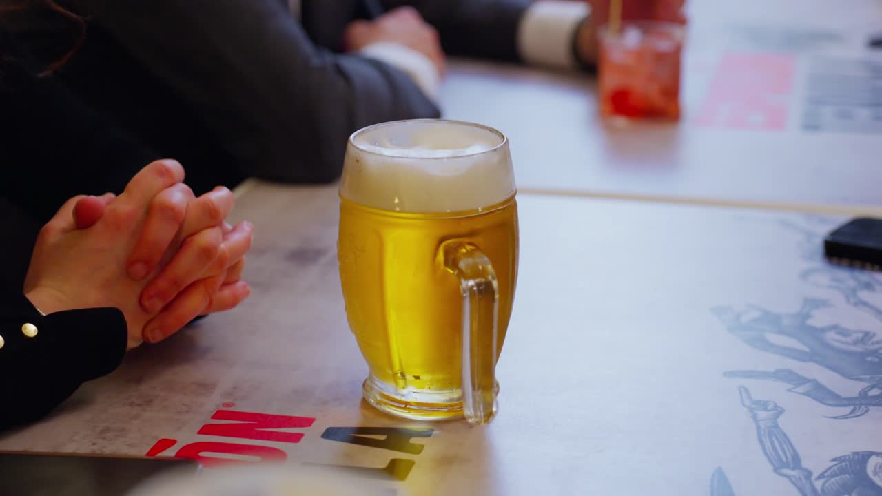 Glass of beer on a table with a person's hands clasped in a bar setting