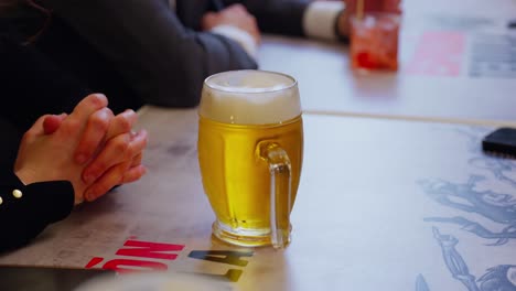 glass of beer on a table with a person's hands clasped in a bar setting