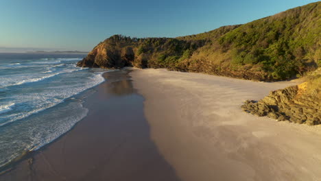 rotating drone shot of man walking along sandy beach at broken head near byron bay