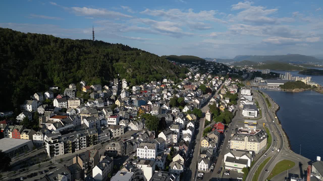 4K drone footage showing the residential part of Ålesund, Norway, near Mount Aksla. The shot captures houses, roads, and coastline on a clear summer day with soft evening light